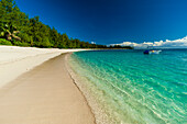 A boat anchored off the shore of a pristine tropical beach. Denis Island, Seychelles.