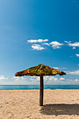 A tiki umbrella on a palm tree trunk on Pinney's white sand beach. Nevis Island, West Indies.