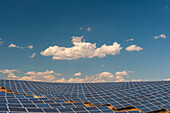 Ein Feld mit Solarmodulen in einem Solarkraftwerk unter blauem Himmel mit weißen Puffwolken. Les Mees, Provence, Frankreich.