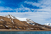 Schneebedeckte Klippen erheben sich hinter einer kleinen Siedlung in der Nähe von Longyearbyen an der Bucht des Adventfjorden. Insel Spitzbergen, Svalbard, Norwegen.