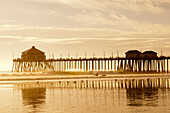 The Huntington Beach Pier and surfers at sunset. Huntington Beach, California.