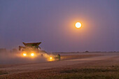 Combine harvesting soybeans as full moon rises (harvest moon), Marion County, Illinois. (Editorial Use Only)