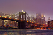 Die Skyline von Manhattan und die Brooklyn Bridge im Dunst der Abenddämmerung.
