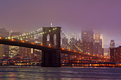 Manhattan skyline and the Brooklyn bridge in the mist at dusk.