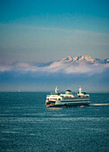 USA, Washington State, Seattle. Ferry sails into Seattle's Elliot Bay in front of morning fog and the Olympic Mountains.