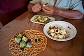 Cropped unrecognizable senior male with knife peeling green fig at table with disposable tray in house room
