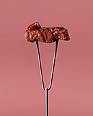 Appetitliches blutiges Steak mit Ketchup auf einer Fleischgabel aus rostfreiem Stahl vor rosa Hintergrund