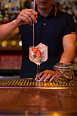 Unbekannter Barkeeper rührt einen Gin-Tonic-Cocktail mit einem Löffel in der Bar