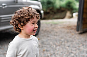 Entzückendes kleines Kind mit lockigem Haar und braunen Augen, das vor einem unscharfen Hintergrund wegschaut