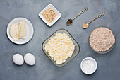 Draufsicht auf verschiedene Produkte für kohlenhydratarme Bagels mit Hüttenkäse und Mozzarellakäse neben Mehl auf einem Tisch mit Gewürzen
