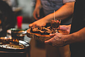 Anonymer Mann mit einem Brett mit gegrilltem Schweinefleisch in der Hand in einem überfüllten Café vor einem unscharfen Hintergrund während des Abendessens