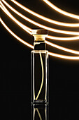 Komposition eines stilvollen Parfümflakons mit goldenem Deckel auf schwarzem Hintergrund in der Nähe von Leuchtstoffröhren
