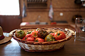 Pile of fresh tomatoes in wicker basket placed on table in rustic kitchen in harvest season