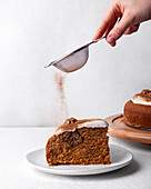 Crop unrecognizable person with sieve sprinkling tasty carrot cake piece with ground cinnamon on light background