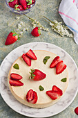Tasty round shaped cheesecake decorated with ripe strawberries and green mint leaves served on plate on table in light kitchen