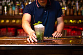 Hand of unrecognizable bartender gives you a well elaborated mojito cocktail in the bar after he finished to prepare it