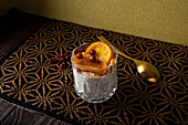 Blick von oben auf ein Glas mit einem Dessert aus Stracciatella-Mousse und Schokoladenspänen, gekrönt von karamellisierten Orangenscheiben und Beeren neben einem Löffel