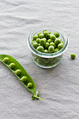 From above of glass small bowl with crispy green peas near pile of crunchy pea pods on table at home