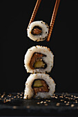 Appetizing fresh sushi rolls served with sesame seeds and chopsticks on black background