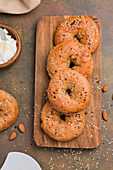 Tasty baked low carbohydrate bagels on wooden cutting board placed on table with almonds and cream cheese in light kitchen