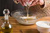 Crop anonymous female breaking raw egg into milk at table with oil and flour while cooking crepes in light kitchen