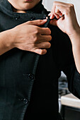 Crop anonymous female buttoning up black jacket of chef uniform while working in modern restaurant