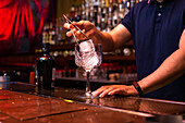 Unbekannter Barkeeper legt einen großen Eiswürfel in das Glas, während er einen Gin-Tonic-Cocktail in der Bar zubereitet