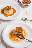 Fresh egg custard topped with sweet dulce de leche served with syrup on wooden table with cutlery in kitchen