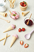 From above of appetizing homemade ice cream scoops in bowl and waffle cones placed on table with strawberries and syrup in kitchen
