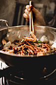 Hand kocht leckeren würzigen Tintenfisch mit gesundem Gemüse in Schüssel mit Stäbchen in asiatischen Restaurant Küche