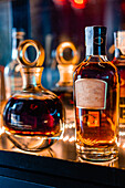 Transparente Glasflaschen mit Whiskey auf dem Tresen einer dunklen Bar bei Nacht