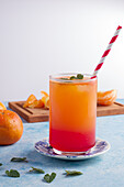 Glass of refreshing Sunrise cocktail with straw served on table with fresh oranges
