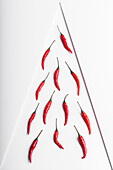 Scharfe rote Chilischoten auf einem Teller vor einem weißen, geometrischen Hintergrund