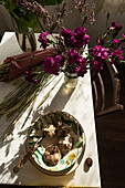 From above of table with garlic in bowl near bunch of cereal grass and glass of blooming flowers in rural house