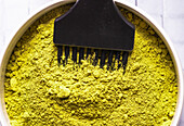 Schale mit getrockneter Lawsonia inermis in Schale mit professionellem Pinsel zum Färben mit natürlichem Öko-Farbstoff in hohem Winkel