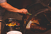 Crop gesichtslose Person mit Zange grillen Fleisch auf Gestell in heißen Grill in der Nähe von Sauce während des Kochvorgangs in hellen Café