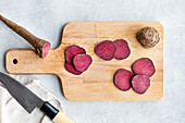 Top view composition of ripe raw beetroot slices placed on wooden cutting board on kitchen table near sharp knife