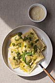 Top view of appetizing cooked ravioli pasta with green sauce and herbs placed on white plate with fork on table