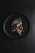 Top view of fresh shimeji mushrooms served on black plate on dark table in studio