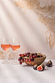 Gläser mit rotem Getränk auf einem Tisch mit einer Schale mit Trauben und Feigen
