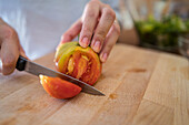 Anonymous female slicing fresh tomato on cutting board while preparing healthy salad in kitchen at home