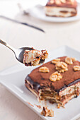 High angle of crop spoon holding delicious tiramisu dessert garnished with walnuts served on white table
