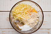 Draufsicht auf eine Glasschüssel mit Mehl und geriebenem Käse für Kürbishäcksel auf einem Holztisch in einer hellen Küche