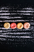 Top view of colored cookies on black background surrounded by strips of sugar