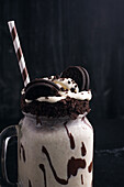 Tasty milkshake with crushed biscuits and straw in glass with chocolate sauce