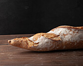 Appetizing freshly baked baguette with crispy crust placed on wooden table against black background