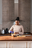 Junge Afroamerikanerin salzt Kochbananen in einer Schüssel, während sie Patacones am Tisch im Haus zubereitet