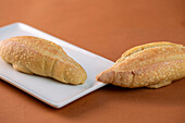 From above white rectangular plate with freshly baked wheat bread loaves placed on brown background