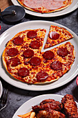 Blick von oben auf einen Teller mit leckerer Peperoni-Pizza und einer Schüssel mit Soße auf einem grauen Tisch beim Mittagessen