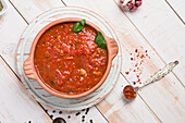 Holzschüssel mit roter Marinara-Soße aus Tomaten mit Basilikumblättern auf dem Tisch mit Knoblauch und Gewürzen